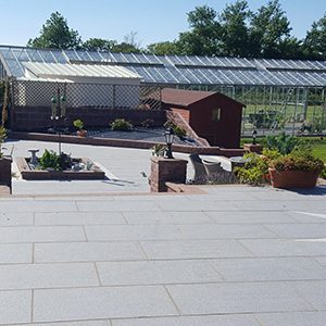 landscaping company in Guernsey. Large modern grey patio area with steps leading down to a big garden and greenhouse