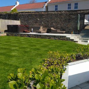 Garden services in Guernsey feature image shows landscaped garden with bespoke paving and stonemasonry flower bed.