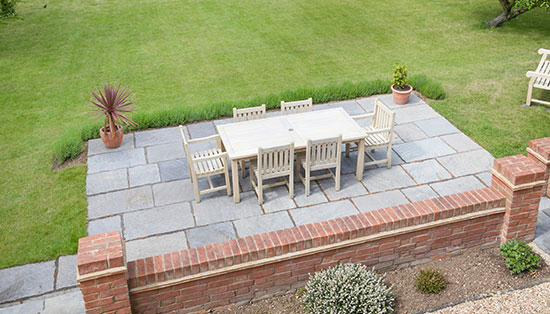 Large Guernsey back garden with lawn and stone patio with wooden patio furniture on a terrace in summer.