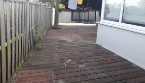 Before photo showing old rotten garden decking with a broken wooden fence.