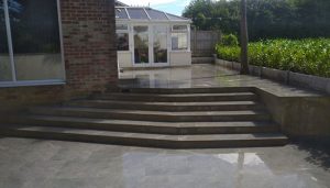Grey Porcelain patio with steps and a new Griselinia hedge planted using rock-face concrete gravel boards has boundaries for a smart and lasting look.